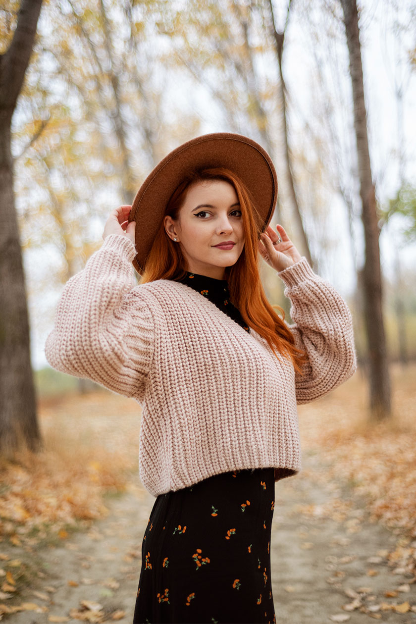 Portrait of a woman in a brown wide-brim hat and pink knit sweater in an autumn park